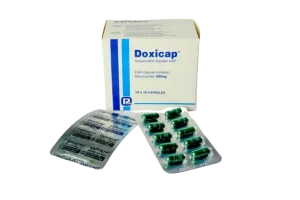 A white box of Doxicap medication next to two blister packs containing green 100mg Doxycycline capsules.