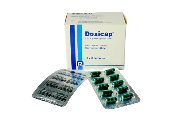 A white box of Doxicap medication next to two blister packs containing green 100mg Doxycycline capsules.