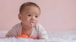 একটি ছোট শিশু বিছানায় শুয়ে মুখ দিয়ে দুধ উগরে দিচ্ছে বা বমি করছে।