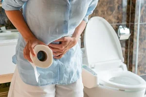 পেটে ব্যথায় কাতর একজন ব্যক্তি বাথরুমে টয়লেট পেপার হাতে দাঁড়িয়ে আছেন।