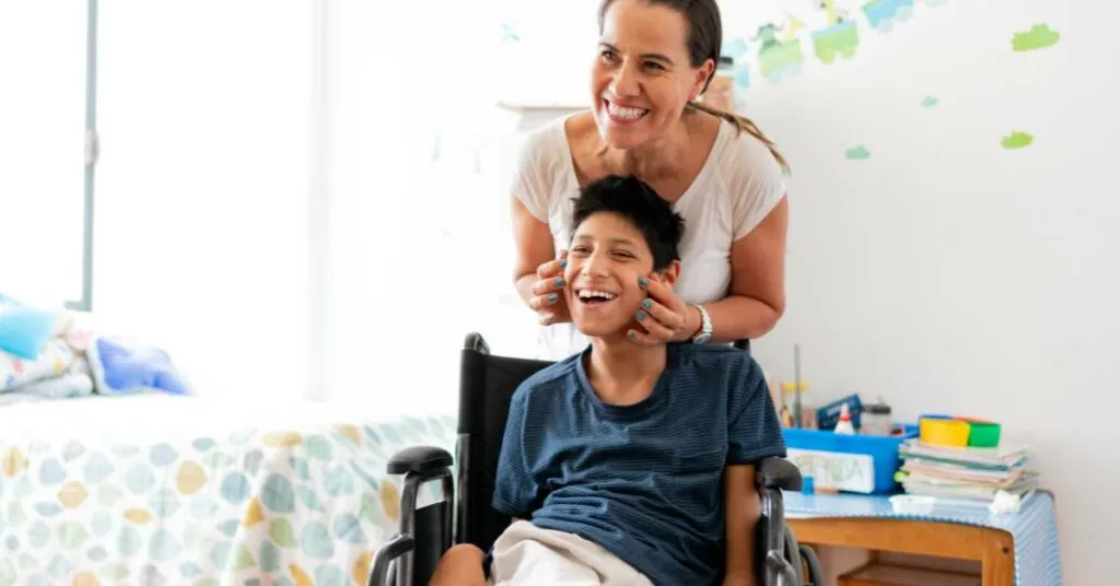 সেরিব্রাল পালসিতে আক্রান্ত একজন হাস্যোজ্জ্বল শিশু হুইলচেয়ারে বসে আছে এবং তার পেছনে একজন যত্নকারী বা মা হাসিমুখে তাকে সহায়তা করছেন।