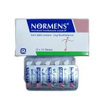 A white Normens tablet box positioned above a silver blister strip showing individual white circular pills.