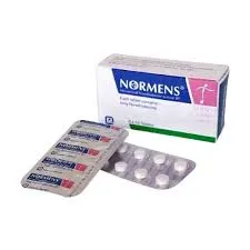 A white and blue box of Normens Norethisterone 5mg tablets resting next to two blister strips containing small white pills.