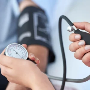 Close-up of a person's hands operating a manual blood pressure cuff and gauge on a patient.