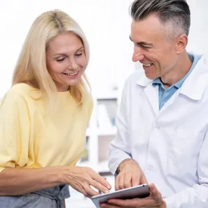 A smiling male doctor and a female patient looking at a digital tablet together during a positive medical appointment.