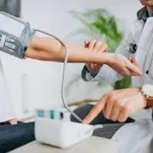 A close-up of a doctor in a white coat using a digital monitor to check a patient's blood pressure in a clinic.