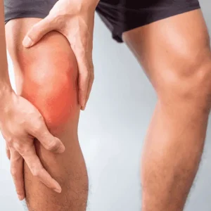 A person wearing black shorts holds their painful knee, which is highlighted with a red glow to indicate inflammation or injury