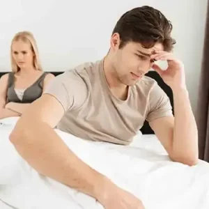 A distressed man sitting on a bed reflecting on personal health challenges.