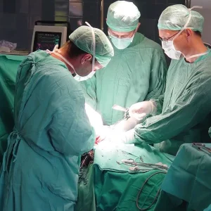 Three surgeons in green scrubs and protective masks work together during a surgical operation in an operating room.