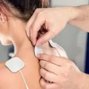 A close-up of a healthcare provider's hands applying white adhesive electrode pads to a woman's upper back and neck for electrotherapy treatment.